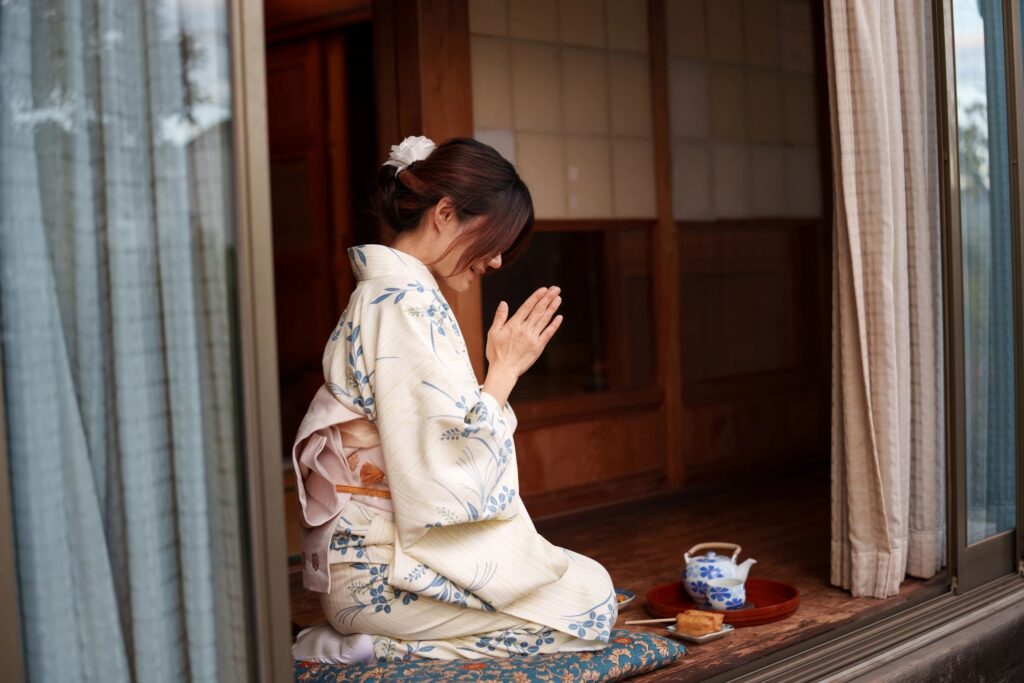 Woman in kimono praying while sitting on engawa veranda